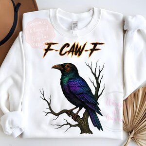 May include: White sweatshirt with a detailed illustration of a crow perched on a branch. The crow has iridescent purple and green feathers. The text "F-CAW-F" is above the crow in a burnt orange font.
