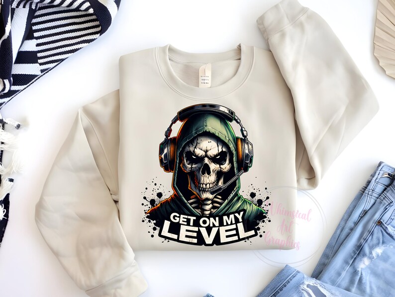 May include: A beige sweatshirt with a graphic print of a skull wearing a green hooded sweatshirt and headphones. The text "Get on my level" is printed below the skull.