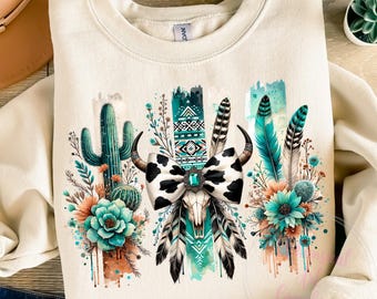 May include: A beige sweatshirt with a graphic design featuring a cow skull with a black and white bow, turquoise feathers, and cactus plants. The design is surrounded by watercolour-style splashes of turquoise, green, and orange.