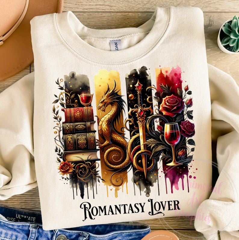 May include: A cream colored sweatshirt with a watercolor design featuring a dragon, a sword, a wine glass, and a stack of books. The design is surrounded by roses and vines. The text "Romantasy Lover" is printed below the design.