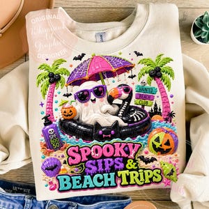 May include: Cream-colored sweatshirt featuring a colorful Halloween-themed graphic. The design includes a ghost wearing sunglasses, a black flamingo float, palm trees, pumpkins, and the text "SPOOKY SIPS & BEACH TRIPS". The design also includes the text "ORIGINAL Whimsical Art Graphics DESIGNER".
