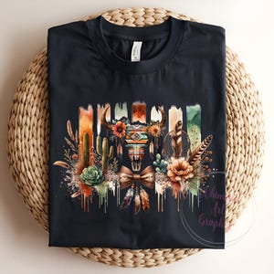 May include: Black t-shirt with a colorful graphic design featuring a skull with feathers, cacti, and flowers. The design has a watercolor effect and is dripping with paint.