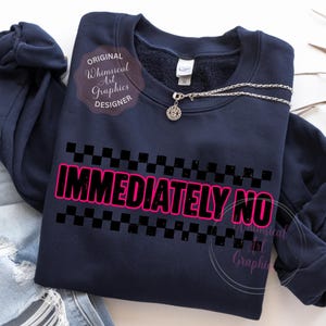 Puede incluir: Sudadera azul marino con el texto "IMMEDIATELY NO" en rosa con contorno negro, encima y debajo del texto patrones de cuadros negros. Un collar plateado con un colgante redondo est&aacute; sobre la sudadera.