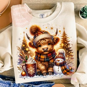 May include: Cream-colored sweatshirt featuring a Highland cow wearing a plaid hat and scarf, alongside a snowman. A mug of hot chocolate and Christmas trees complete the winter scene. The text "ORIGINAL Whimsical Art Graphic DESIGNER" is visible.