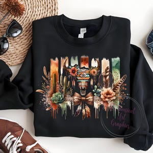 May include: Black sweatshirt with a colorful graphic print of a skull with feathers, cacti, and flowers. The graphic has a southwestern theme.