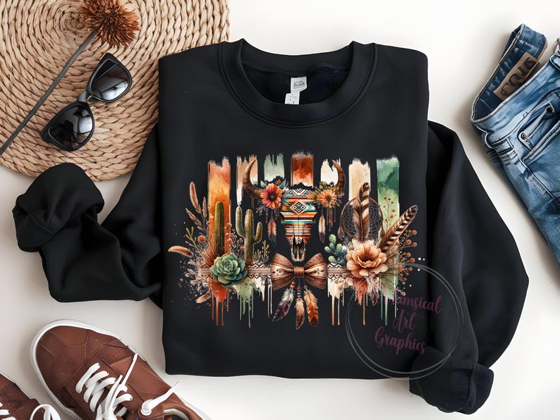 May include: Black sweatshirt with a colorful graphic print of a skull with feathers, cacti, and flowers. The graphic has a southwestern theme.