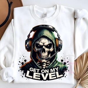 May include: White sweatshirt with a graphic of a skeleton wearing a green hooded sweatshirt and headphones. The text "Get on my level" is printed below the graphic.