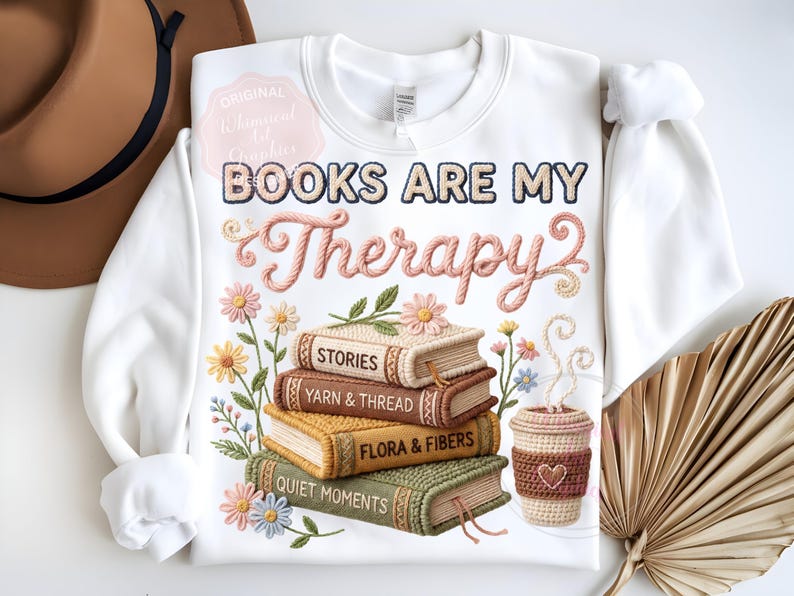 May include: White sweatshirt with the embroidered phrase "BOOKS ARE MY Therapy" and a stack of books with floral accents. The books are labeled "STORIES", "YARN & THREAD", "FLORA & FIBERS", and "QUIET MOMENTS". A coffee cup is also featured.