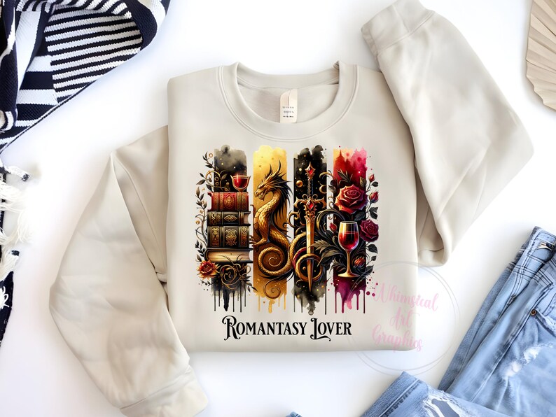 May include: A beige sweatshirt with a graphic print of a dragon, a sword, a glass of wine, and a stack of books. The graphic is surrounded by watercolor-like drips. The text "Romantasy Lover" is printed below the graphic.