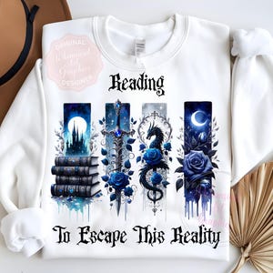 May include: White sweatshirt with a fantasy-themed design. The design includes the word "Reading" above four vertical panels with images of a castle, sword, dragon, and rose. The text "To Escape This Reality" is below the panels.