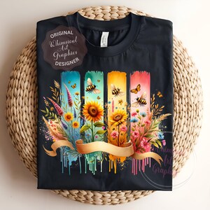 May include: Black t-shirt featuring a colorful floral and bee design. The design includes sunflowers, wildflowers, and bees on vertical panels with a gold ribbon. The text "ORIGINAL Whimsical Art Graphics DESIGNER" is also visible.