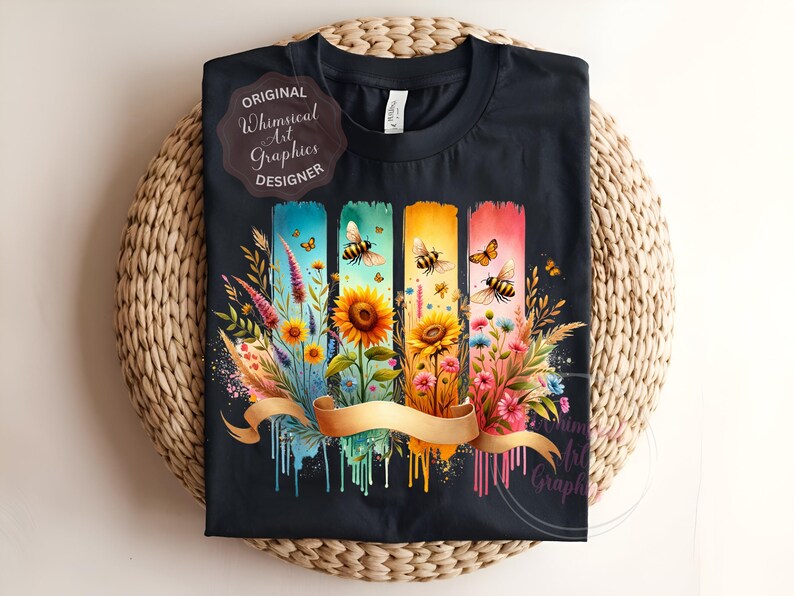 May include: Black t-shirt featuring a colorful floral and bee design. The design includes sunflowers, wildflowers, and bees on vertical panels with a gold ribbon. The text "ORIGINAL Whimsical Art Graphics DESIGNER" is also visible.