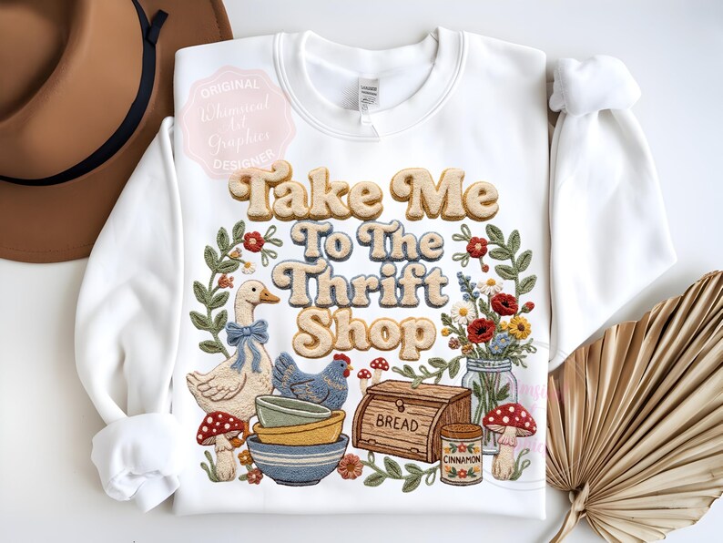 Puede incluir: Sudadera blanca con la frase "Take Me To The Thrift Shop" en una fuente retro. El dise&ntilde;o incluye un ganso, una gallina, cuencos, pan, flores y setas, rodeados por una corona floral.
