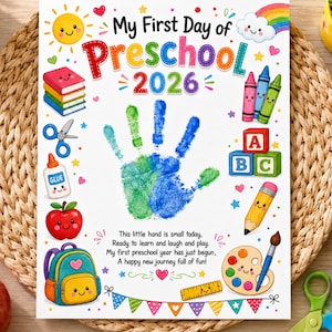 May include: A white rectangular sign featuring the text My First Day of Preschool 2026, a central green and blue handprint, and colorful illustrations of books, crayons, ABC blocks, a glue bottle, an apple, a backpack, a pencil, and a paint palette.