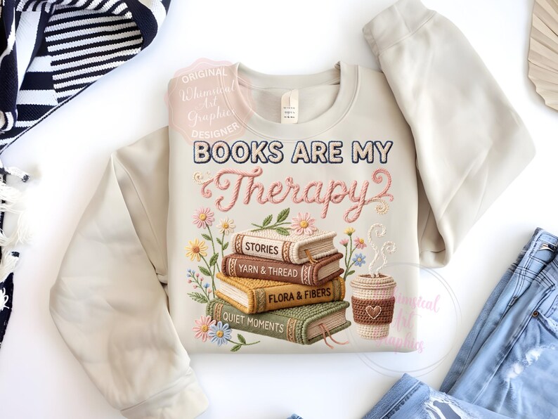 May include: Beige sweatshirt with the embroidered text "BOOKS ARE MY Therapy" and a stack of books with floral accents. The books are labeled "STORIES", "YARN & THREAD", "FLORA & FIBERS", and "QUIET MOMENTS". A coffee cup is also featured.