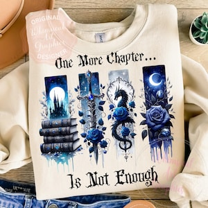 Puede incluir: Sudadera crema con un diseño de fantasía. El diseño presenta ilustraciones de castillo, espada, dragón y rosas en tonos azules, con el texto "One More Chapter... Is Not Enough".