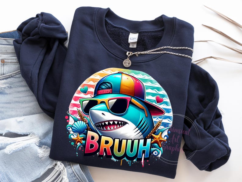 Puede incluir: Sudadera azul marino con un tibur&oacute;n de dibujos animados con gafas de sol y una gorra colorida. El gr&aacute;fico del tibur&oacute;n incluye la palabra "BRUUH" en colores arco&iacute;ris. El dise&ntilde;o incorpora corazones, conchas marinas y estrellas de mar. Un collar plateado con un colgante est&aacute; sobre la sudadera.