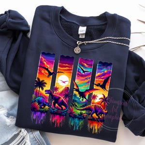 May include: Navy blue sweatshirt featuring a vibrant, colorful graphic of dinosaurs and a sunset scene. The design includes palm trees, pterodactyls, and various dinosaur species. The text "Whimsical Art Graphic" is visible on the lower right.