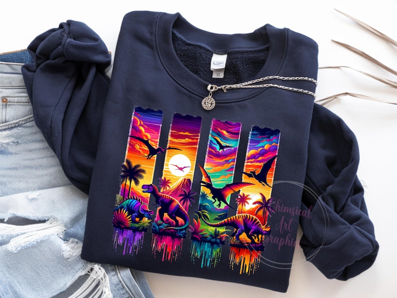 May include: Navy blue sweatshirt featuring a vibrant, colorful graphic of dinosaurs and a sunset scene. The design includes palm trees, pterodactyls, and various dinosaur species. The text "Whimsical Art Graphic" is visible on the lower right.