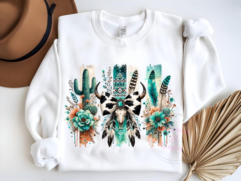 May include: White sweatshirt featuring a graphic print of a cow skull with a bow, cactus, and feathers in shades of green, blue, and orange.