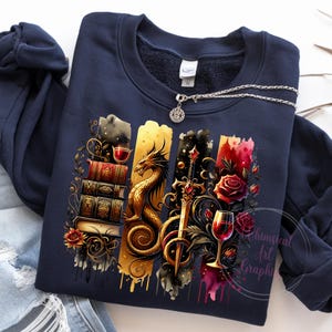 May include: A navy blue sweatshirt with a graphic print of a dragon, a sword, a wine glass, and a stack of books. The graphic is in shades of gold, red, and black.