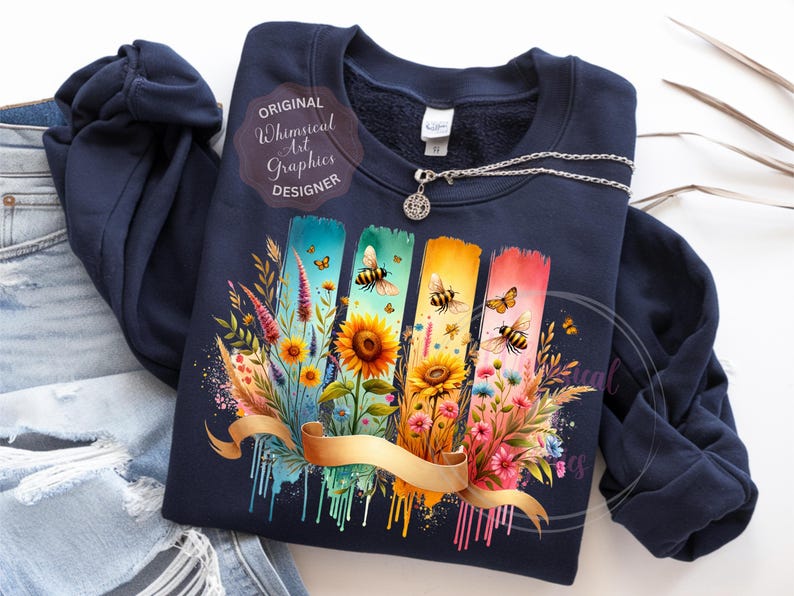 May include: Navy blue sweatshirt featuring a colorful floral design with bees, sunflowers, and butterflies. The design includes vertical brushstrokes in blue, green, yellow, and pink, with a gold ribbon. The text "Original Whimsical Art Graphics Designer" is also visible.
