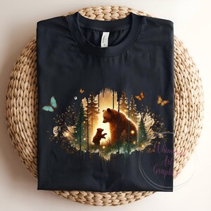 May include: A black t-shirt with a graphic print of a mother bear and her cub standing in a forest setting. The graphic is surrounded by butterflies and a soft glow.