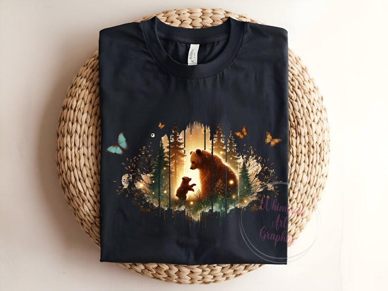 May include: A black t-shirt with a graphic print of a mother bear and her cub standing in a forest setting. The graphic is surrounded by butterflies and a soft glow.