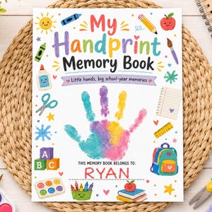 May include: A white memory book titled My Handprint Memory Book with the text Little hands, big school-year memories and This memory book belongs to: RYAN. The cover features a colorful handprint, a sun, apple, pencil, glue, scissors, and backpack.