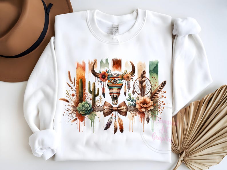 May include: White sweatshirt with a watercolor design of a skull with feathers, cacti, and flowers. The skull is decorated with geometric patterns and a bow tie.