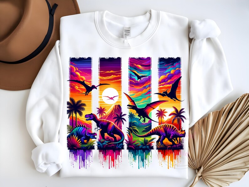 May include: White sweatshirt featuring a colorful dinosaur design. The graphic includes various dinosaurs, palm trees, and flying pterodactyls set against a vibrant sunset backdrop. The design is rendered in shades of purple, orange, and blue.