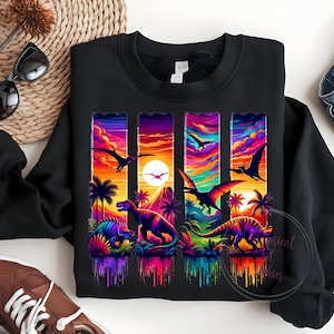 May include: Black sweatshirt featuring a vibrant, colorful graphic of dinosaurs and pterodactyls against a sunset backdrop. The design includes palm trees and a mountain silhouette, with a rainbow-colored, dripping effect at the bottom.