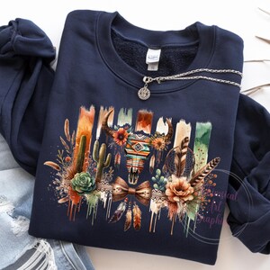 May include: A navy blue sweatshirt with a colorful graphic print of a skull with feathers, cacti, and flowers. The graphic has a southwestern theme.
