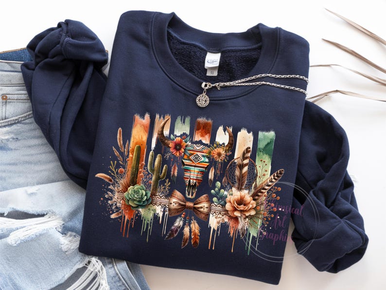 May include: A navy blue sweatshirt with a colorful graphic print of a skull with feathers, cacti, and flowers. The graphic has a southwestern theme.