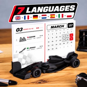 Könnte beinhalten: Ein Tischkalender für März 2027 mit einem schwarzen, 3D-gedruckten Formel-1-Auto als Basis. Der Kalender zeigt die Rennpläne für Sakhir und Dschidda sowie eine Kopfzeile mit 7 LANGUAGES und verschiedenen Nationalflaggen darüber.