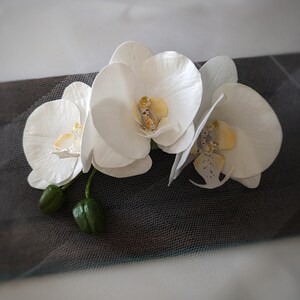 Op de afbeelding: Drie witte orchidee&euml;n met gele centra, gerangschikt op een zwart-wit gepatroneerde stof.