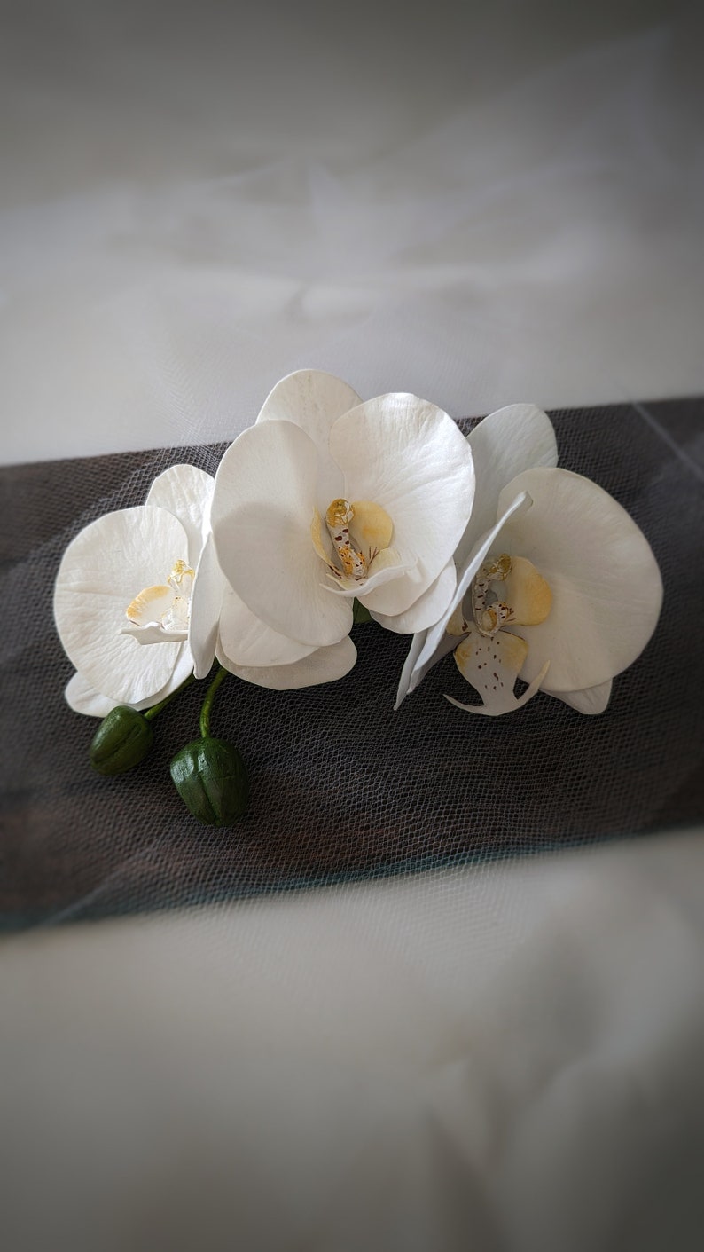 Op de afbeelding: Drie witte orchidee&euml;n met gele centra, gerangschikt op een zwart-wit gepatroneerde stof.