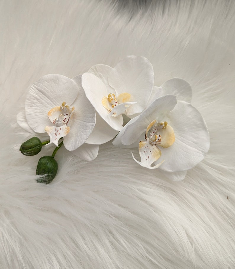 Op de afbeelding: Drie witte orchidee&euml;n met gele centra en bruine markeringen op een wit, pluche oppervlak.