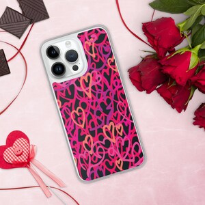 Puede incluir: Una funda transparente para teléfono con fondo negro y un patrón de corazones rosas, rojos y morados.