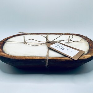 May include: A white candle in a wooden dough bowl with a brown paper tag that says "Artisan Bread". The candle is tied with twine.