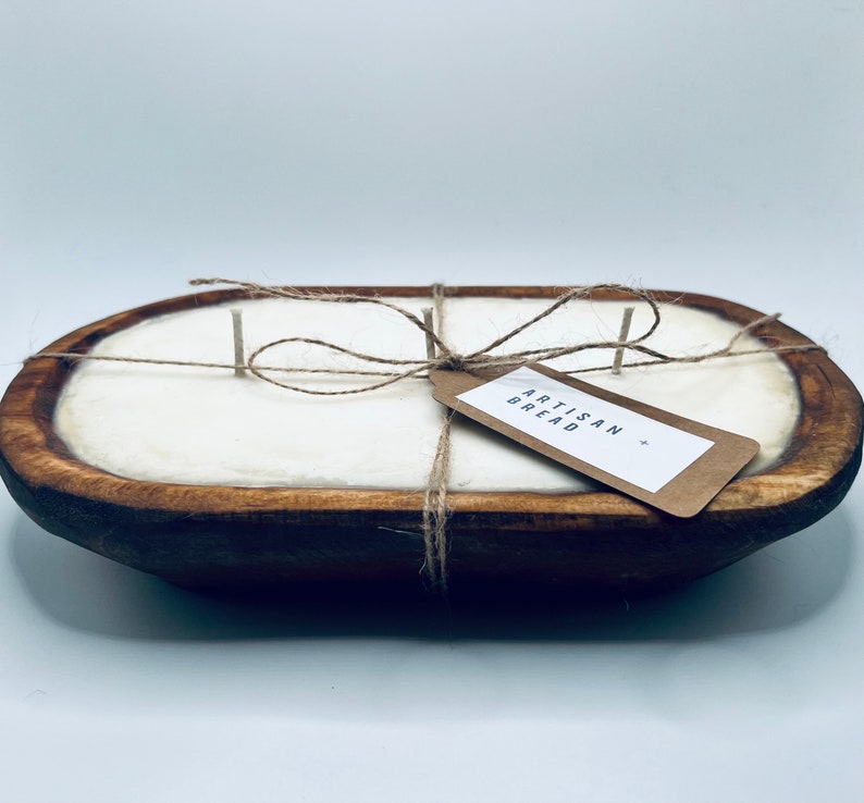 May include: A white candle in a wooden dough bowl with a brown paper tag that says "Artisan Bread". The candle is tied with twine.