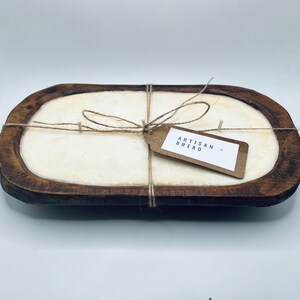 May include: A wooden bread bowl with a white candle inside. The candle is tied with twine and a brown paper tag that says "Artisan Bread".