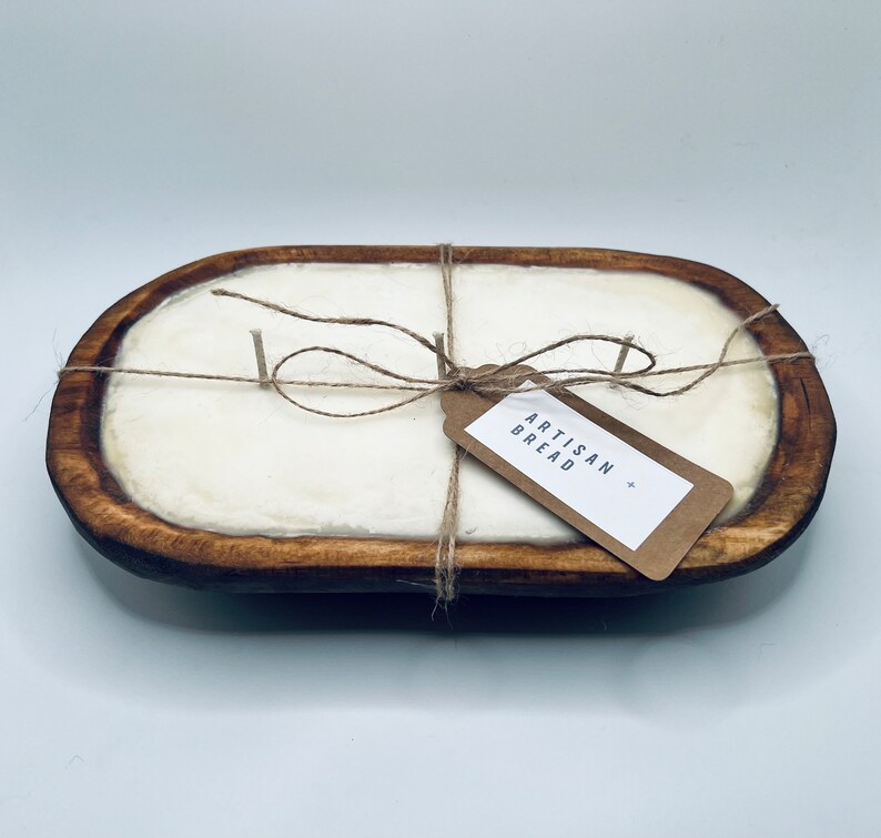 May include: A wooden bread bowl with a white candle inside. The bowl is tied with twine and a brown paper tag that says "Artisan Bread".