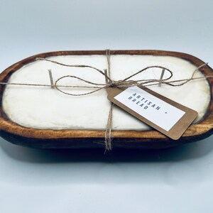 May include: A white candle in a wooden dough bowl with a twine bow and a tag that reads "Artisan Bread".