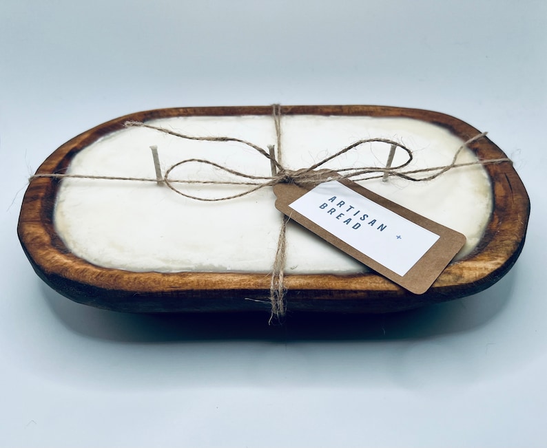 May include: A white candle in a wooden dough bowl with a twine bow and a tag that reads "Artisan Bread".