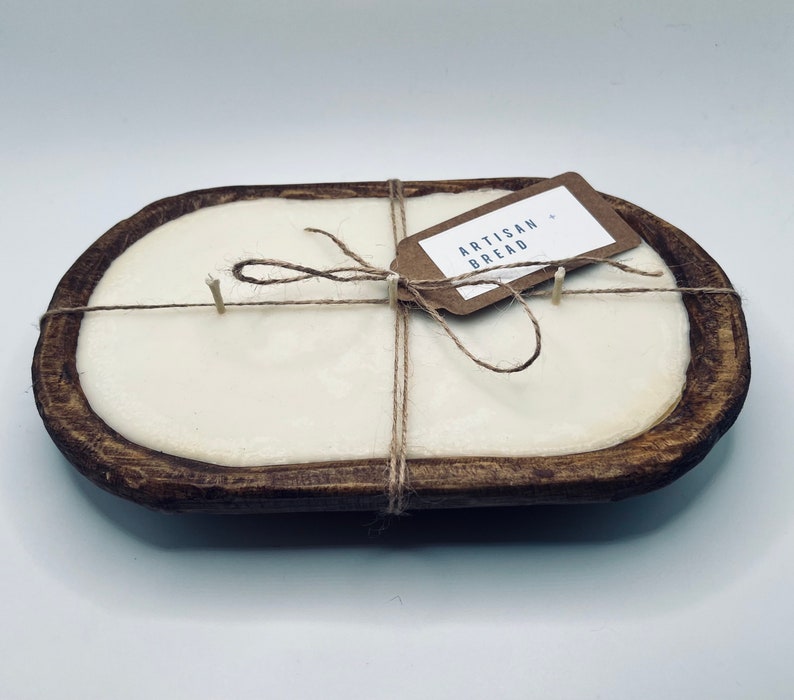 May include: A white candle in a wooden dough bowl with a brown tag that says "Artisan Bread". The candle is tied with twine.