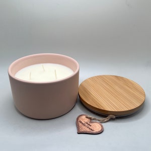 Op de afbeelding: Een roze keramische kaars pot met een houten deksel en een hartvormig label met de tekst "Scented Vanilla Caramel".