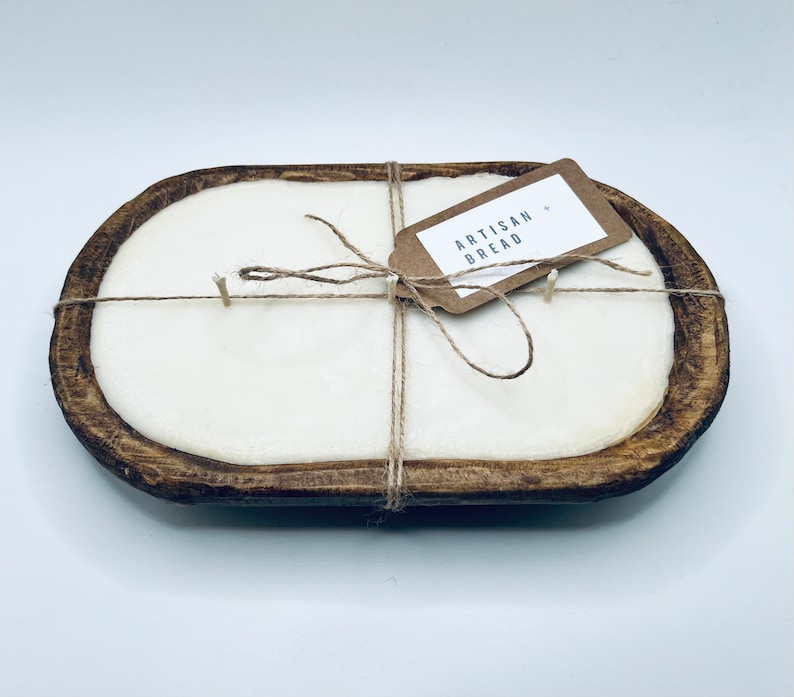 May include: A white candle in a wooden dough bowl with a brown paper tag that says "Artisan Bread". The candle is tied with twine.