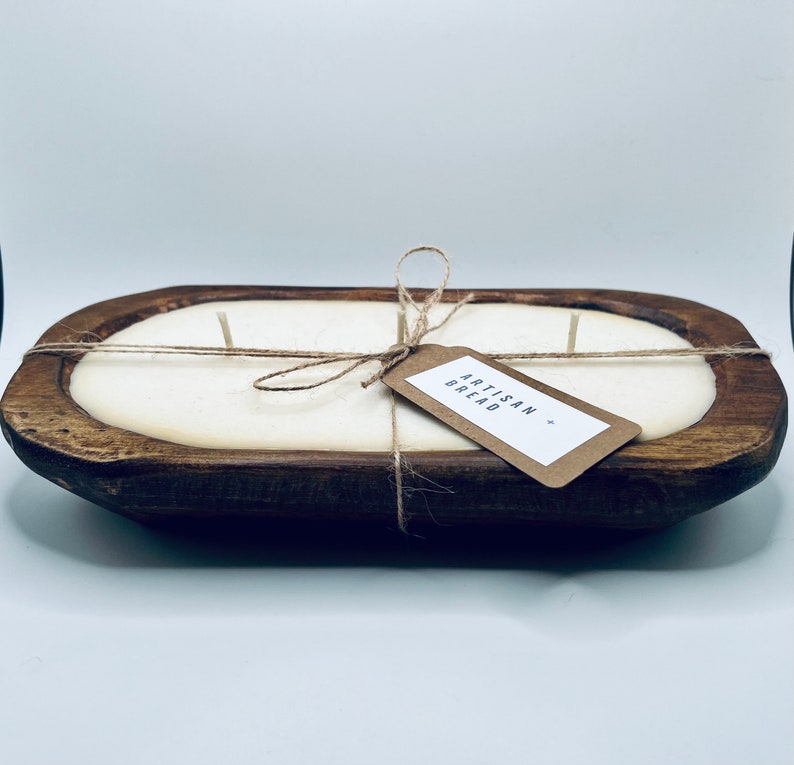 May include: A white candle in a wooden bread bowl with a brown paper tag that says "Artisan Bread".