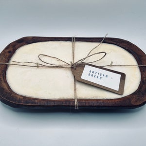 May include: A wooden bread bowl with a white interior, tied with twine and a brown paper tag that reads "Artisan Bread".